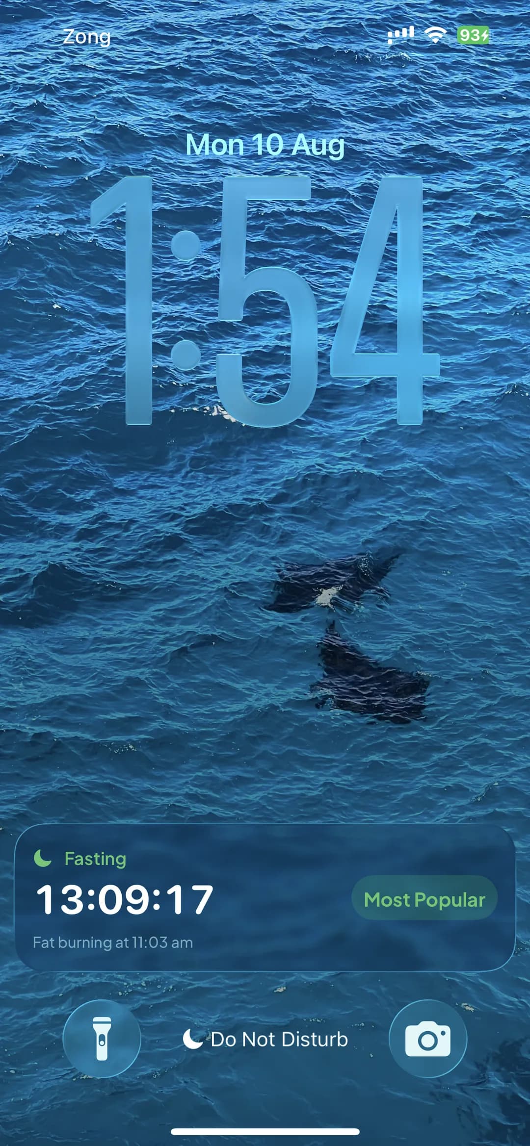 A SlimAI fasting Live Activity on an iPhone lock screen: a Fasting label with a moon icon, a live 13:09:17 countdown, the plan name Most Popular, and the line “Fat burning at 11:03 am”